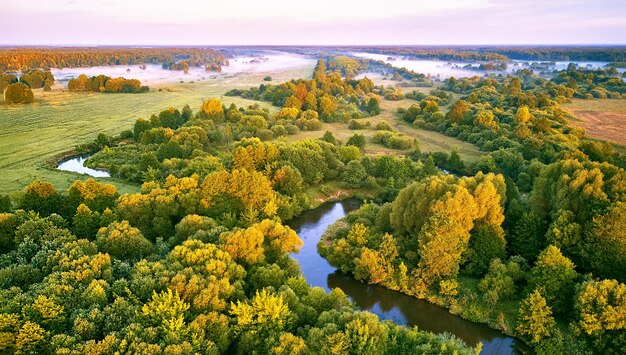 Aerial summer sunrise view Rural landscape river meandering in forest green trees Morning Misty Scene Serene atmosphere fog panorama Agriculture fields wood on riverbank Beauty of nature