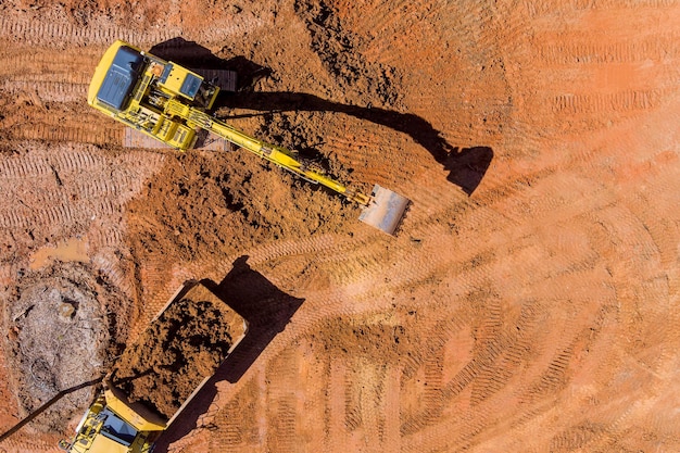 Aerial top down view of an excavator loading earth into a dump truck in a under construction site