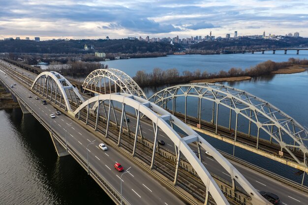 Aerial top view of automobile and railroad Darnitsky bridge across Dnieper river from above, Kiev city skyline