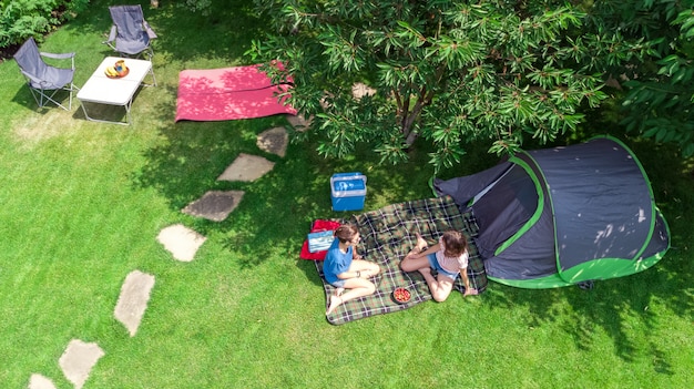 Vista superiore aerea del campeggio da sopra, madre e figlia divertendosi, tenda e attrezzatura di campeggio sotto l'albero, vacanza di famiglia nel concetto del campo all'aperto