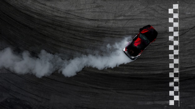 Aerial top view car drifting on race track with finish line and lots of smoke from burning tires.