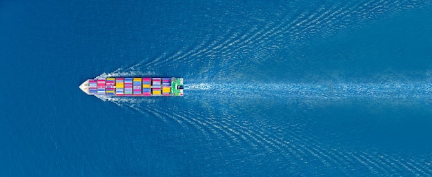 Aerial top view of cargo maritime ship with contrail in the\
ocean ship carrying container and running for export concept\
technology freight shipping sea freight by express ship