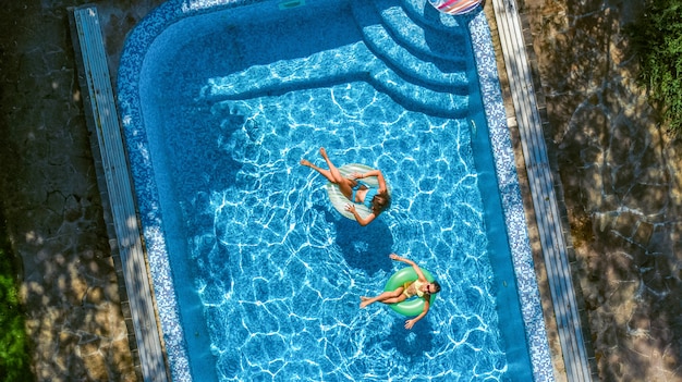 Vista aerea dall'alto di bambini in piscina dall'alto, bambini felici nuotano su ciambelle gonfiabili e si divertono in acqua durante le vacanze in famiglia sul resort