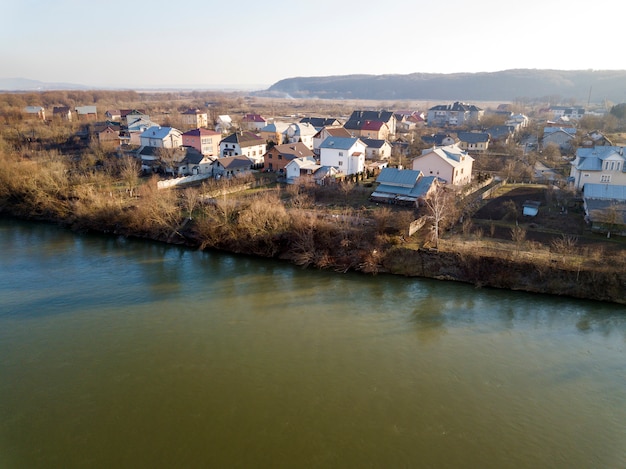 Aerial top view, countryside panorama of residential houses on river bank on blue sky and woody hill. Drone photography.