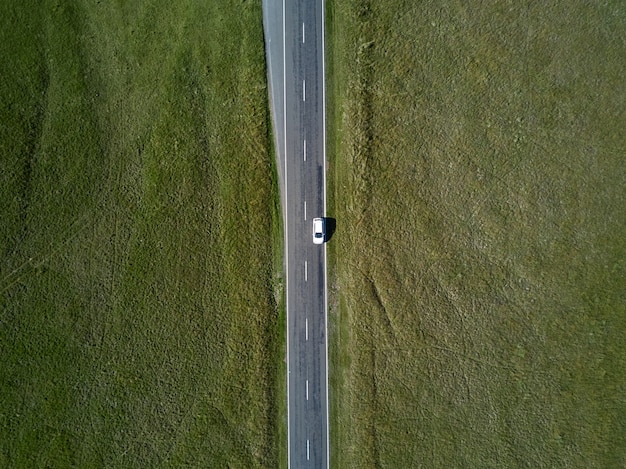 両側に緑の草があるまっすぐな道路に乗っている車からの空中上面図