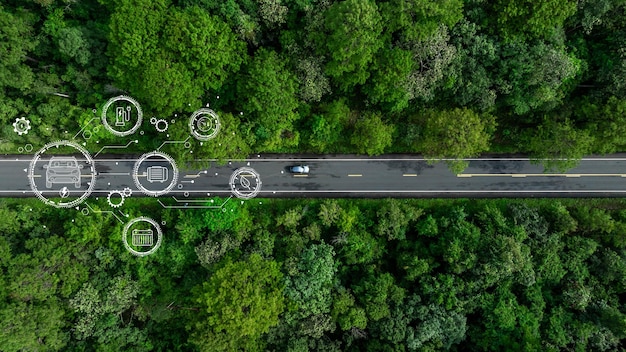 Aerial top view of green electric vehicle car driving over straight forest road EV car electric
