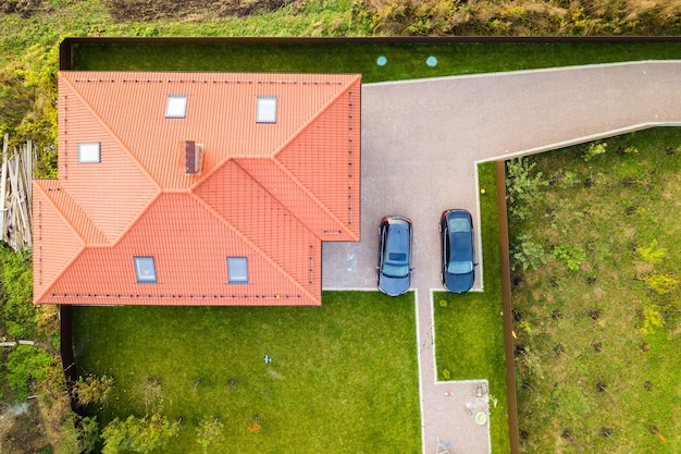 Vista aerea dall'alto del tetto in scandole di casa con finestre a soffitta e auto su cortile lastricato con prato verde.