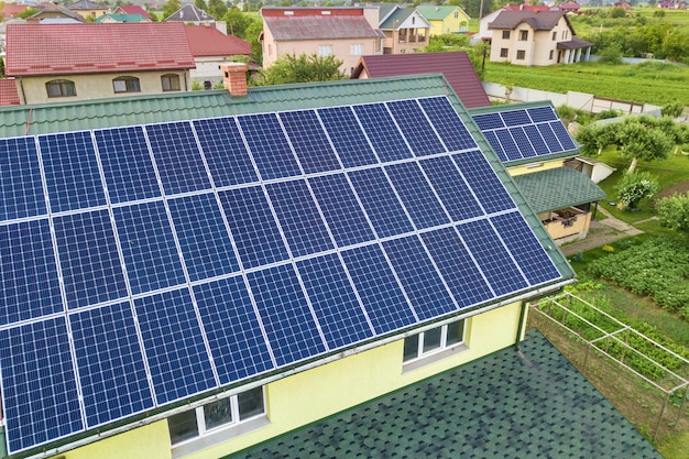 Aerial top view of new modern residential house cottage with blue shiny solar photo voltaic panels system on roof. Renewable ecological green energy production concept.