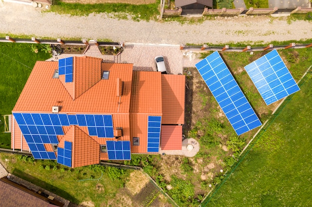 Воздушный взгляд сверху нового современного жилого коттеджа дома с голубой сияющей солнечной системой фотоэлектрических панелей на крыше. Концепция производства экологически чистой зеленой энергии.