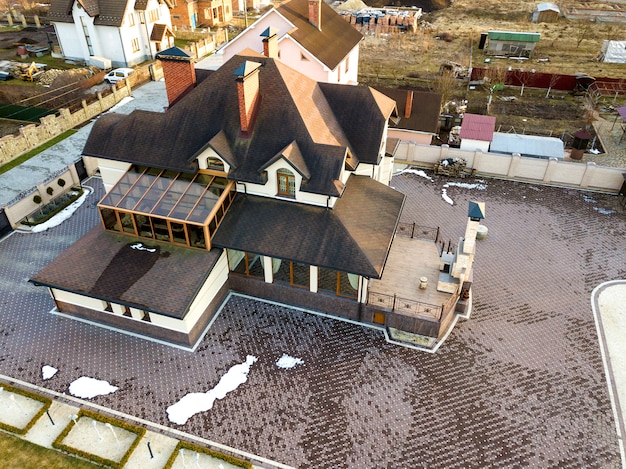 Aerial top view of new residential house cottage with shingle roof on fenced big yard on sunny day.