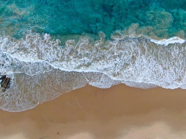 Aerial top view of the ocean colorful waves washing on the\
coast of the pacific ocean california