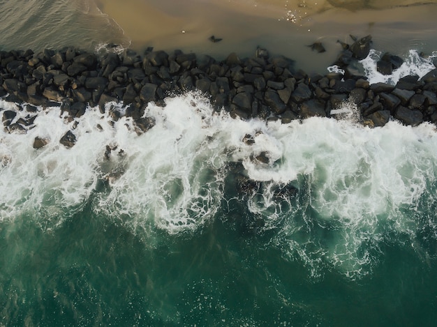 Aerial top view of sea waves hitting rocks on the beach in Italy. Azure clean wavy sea water.