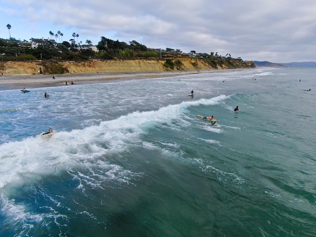 Aerial top view of surfers waiting the waves in blue water. Del Mar Beach, California, USA.