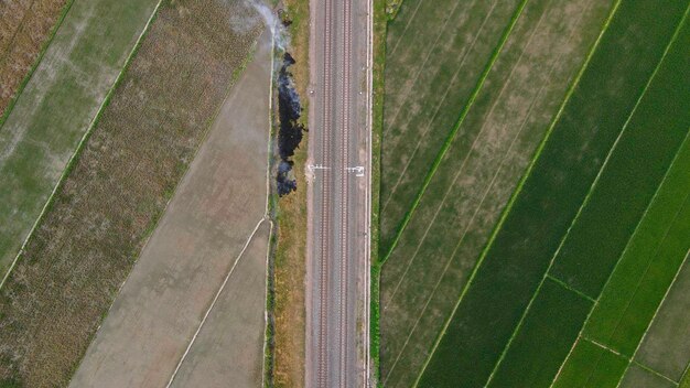 Aerial top view of train rail tracks with rice field around or green country field it in Indonesia