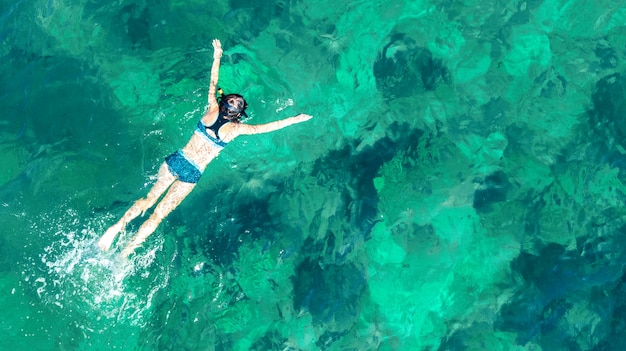 Aerial top view of woman snorkeling from above, girl snorkeler swimming in a clear tropical sea water with corals during summer vacation in Thailand