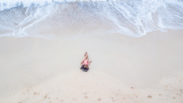 Aerial top view young woman in a bikini lying on the sand and waves.