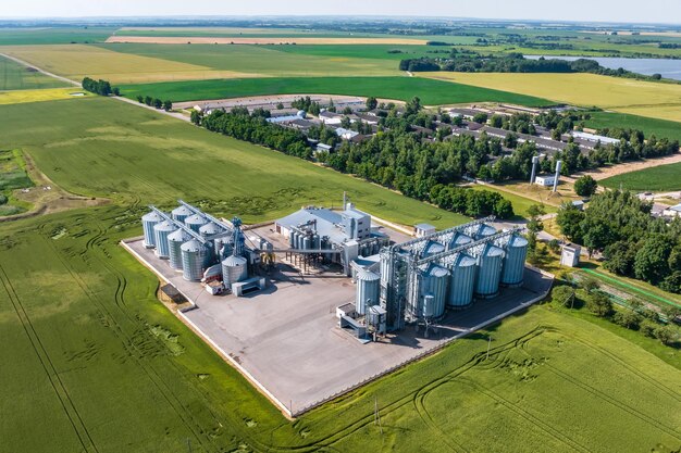 Aerial view on agro silos granary elevator with seeds cleaning line on agroprocessing manufacturing plant for processing drying cleaning and storage of agricultural products in rye or wheat field