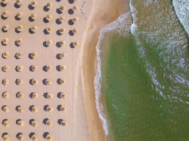 Aerial view of an amazing empty sand beach with straw beach umbrellas and turquoise clear water