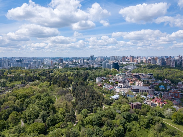 Aerial view of beautiful big green botanical garden in summer, city buildings on horizon with clouds in sky