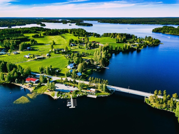 Photo aerial view beautiful summer landscape with blue lake green fields small town with wooden houses and fishing boats on the shore of water countryside road with bridge in finland