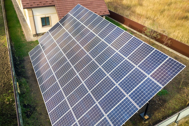 Аэрофотоснимок большой голубой панели солнечных батарей установлен на земле структуры возле частного дома.
