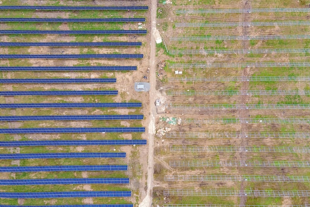 Aerial view of big electric power plant construction with many rows of solar panels on metal frame for producing clean ecological electrical energy. Development of renewable electricity sources.