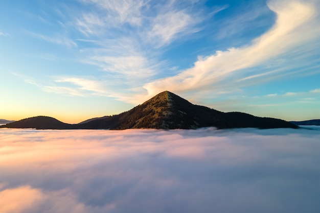 明るい日の出の白い密な雲の上の大きな山の空撮。