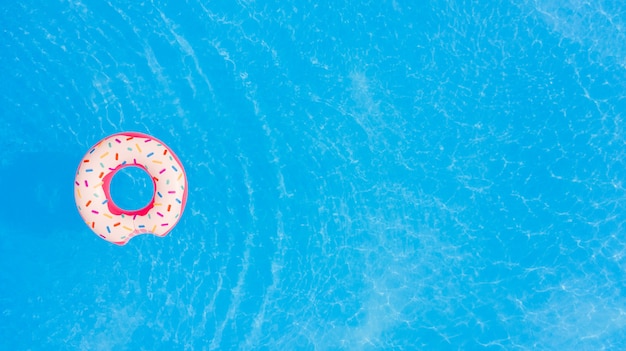 Aerial view of big pink donut in the swimming pool background