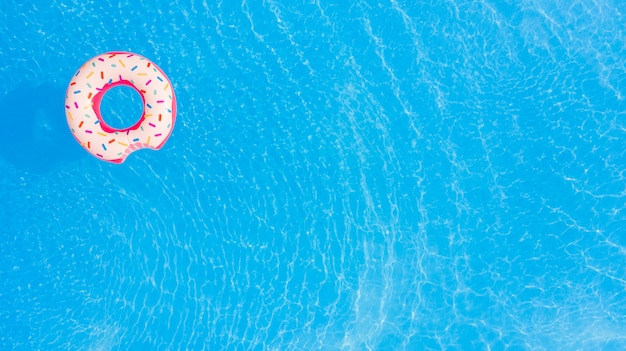 Aerial view of big pink donut in the swimming pool background