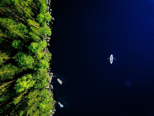 Aerial view of blue lake with a fishing boat and green forests with rocks on a summer day in Finland