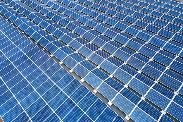 Aerial view of blue photovoltaic solar panels mounted on industrial building roof for producing green ecological electricity. Production of sustainable energy concept.