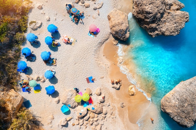 Aerial view of blue sea sandy beach with umbrellas stones and rocks in water at sunset in summer Lefkada island Greece Tropical landscape with sea coast swimming people blue water Top view