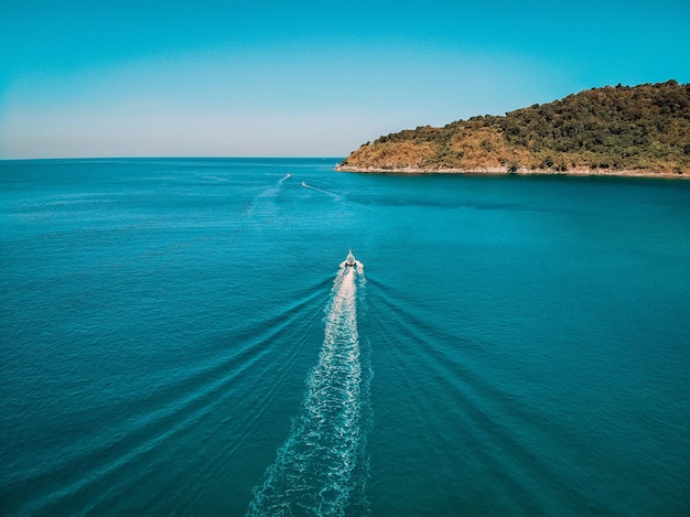 Aerial view, boat is going at full speed in clear blue water right in the middle of the sea