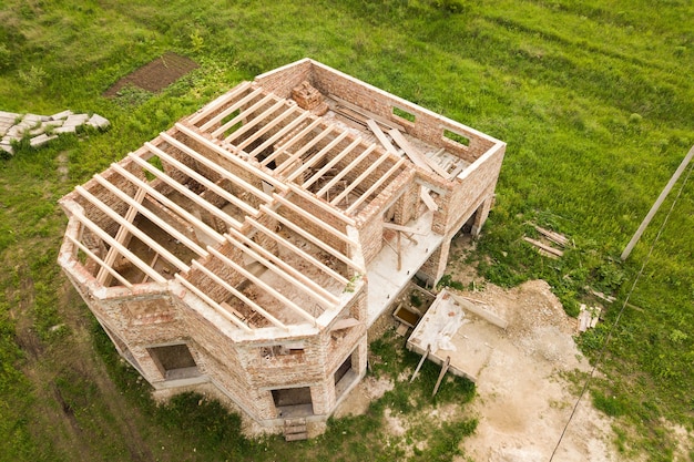 Aerial view of a brick house with wooden ceiling frame under construction.