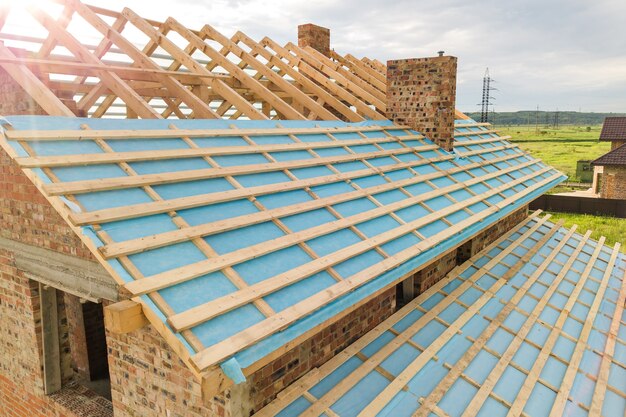 Aerial view of a brick house with wooden roof frame under construction.