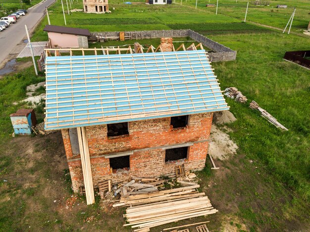 Aerial view of a brick house with wooden roof frame under construction.