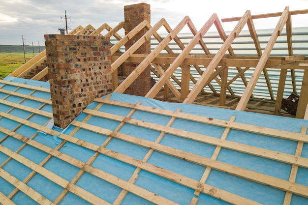 Вид с воздуха на строящийся кирпичный дом с деревянным каркасом крыши.