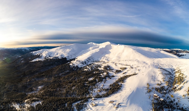 Aerial view of a bright beautiful panorama of a skiing hillside with fir trees and snow on a sunny frosty day with smoky clouds. Nordic Beauty Concept.