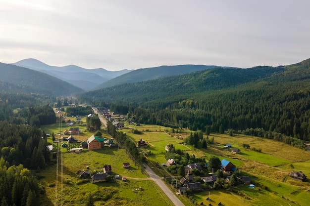 Aerial view of bright foggy morning over small rural homes\
between dark peaks with mountain forest trees at autumn sunrise\
beautiful scenery of wild woodland at dawn