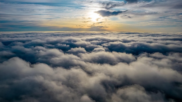 Aerial view of bright yellow sunset over white dense clouds with blue sky overhead