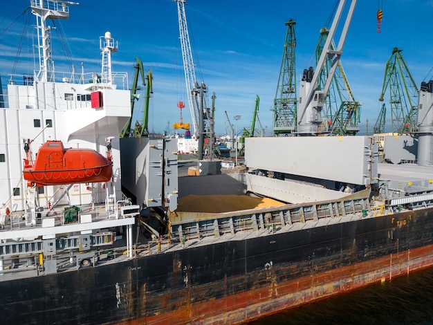 Aerial view of a bulk carrier ship loaded with grain is docked at a busy port with workers and machinery seen in the background