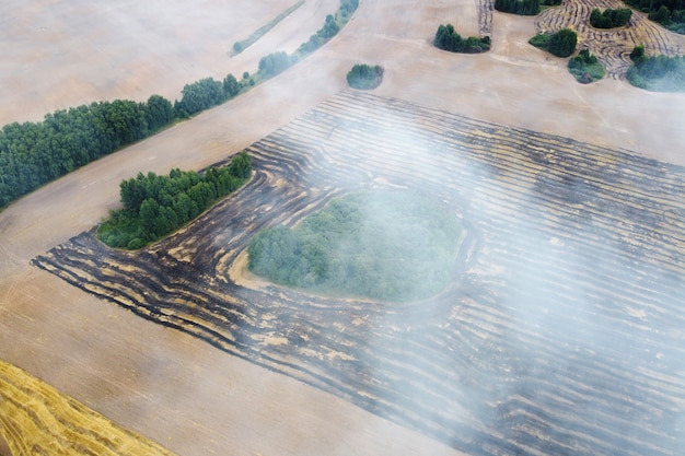 Aerial view of burning field with smoke in farm land