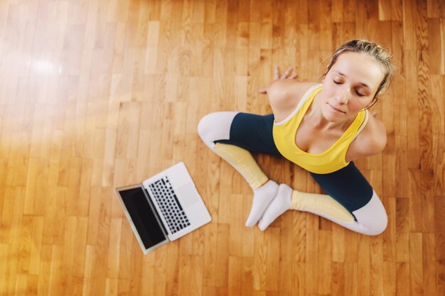 Aerial view of calm woman sitting in lotus yoga pose, meditating and following online class.