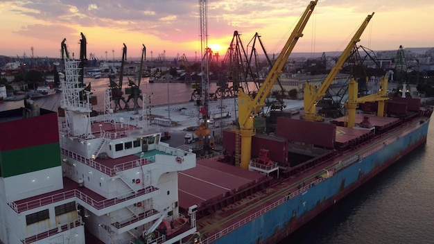 Aerial view of cargo ship bulk carrier is loaded with grain of wheat in port at sunset