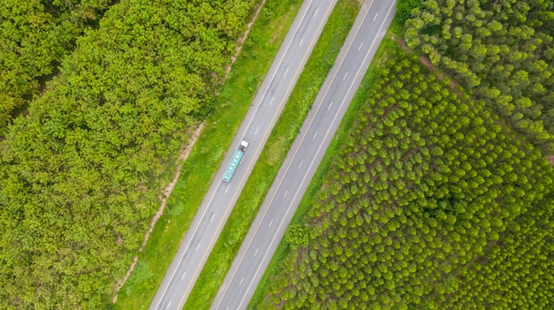 Aerial view of cars and trucks on asphalt road passes through the green forest