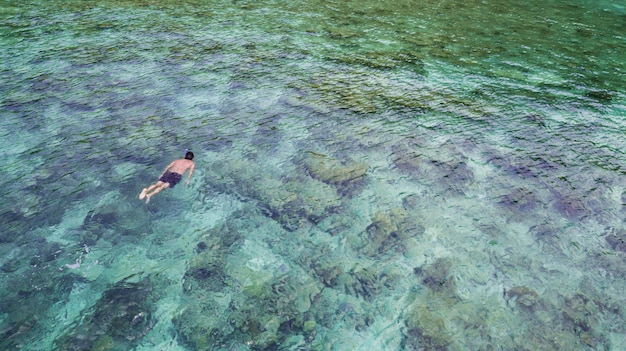 Aerial view of caucasian tourist snorkeling in crystal turquoise water and coral reefs near Perhentian Island.