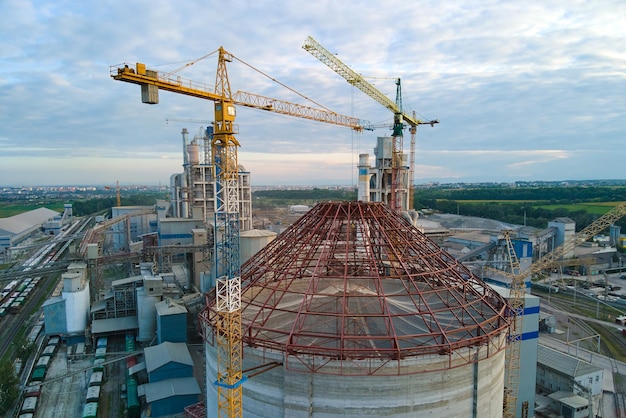 Aerial view of cement factory under construction with high concrete plant structure and tower cranes at industrial production area. Manufacture and global industry concept.