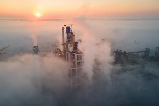 Aerial view of cement factory with high concrete plant structure and tower crane at industrial manufacturing site on foggy evening Production and global industry concept