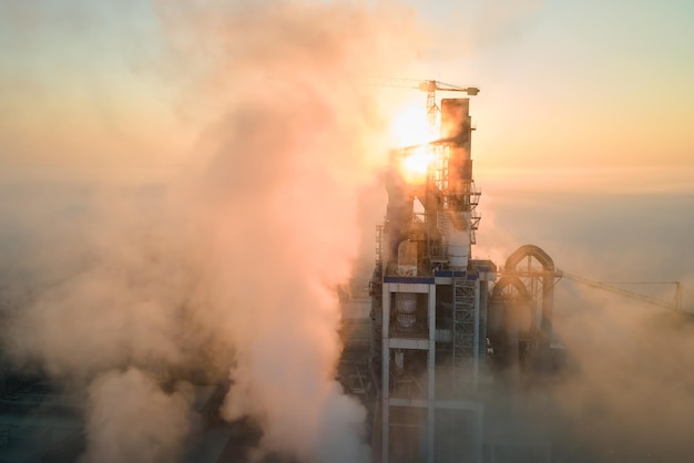 Aerial view of cement factory with high concrete plant structure and tower crane at industrial production site on foggy morning Manufacture and global industry concept