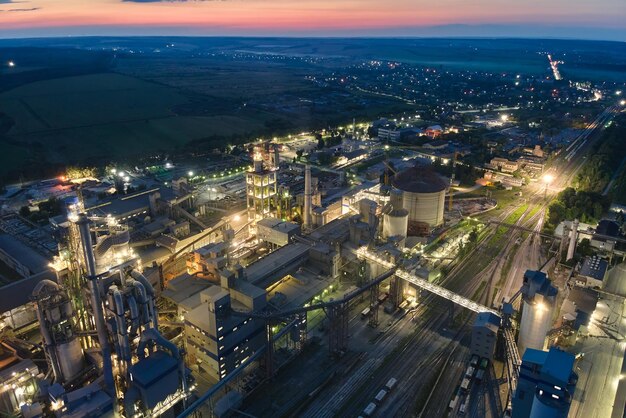 Aerial view of cement factory with high concrete plant structure and tower cranes at industrial production area at night. Manufacture and global industry concept.